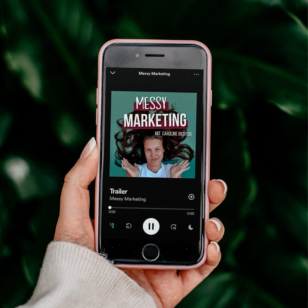 Hand, die Smartphone hält, auf dem der Messy Marketing Podcast abgespielt wird
